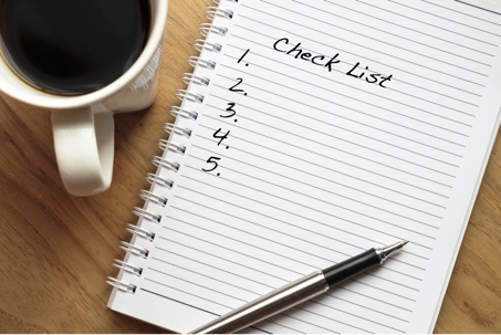 A checklist on lined paper with a pen and a cup of coffee.