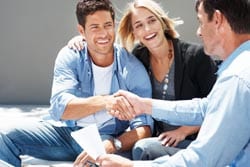 A couple shakes hands with an advisor, all smiling and sitting outside.