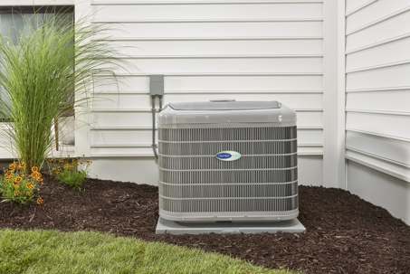 A Carrier air conditioner unit sits on a concrete pad beside a home.