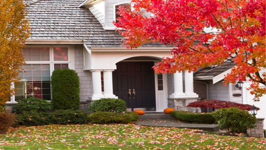 A suburban home exterior features fall colors, with orange pumpkins at the entry.