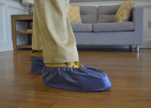 A person wears disposable shoe covers indoors, with a couch in the background.