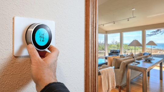 A hand adjusts a smart thermostat on a wall. The display reads "Cool 72".