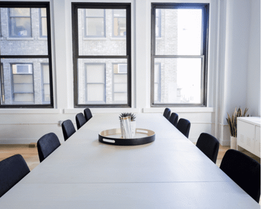 A conference room features a long white table surrounded by black chairs.