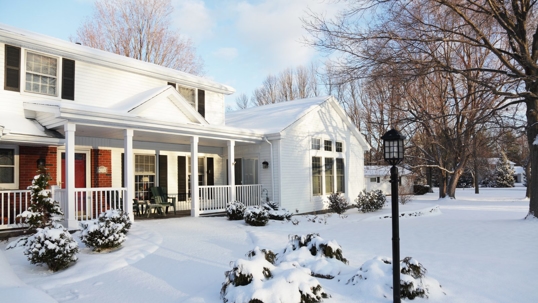 A white two-story house is shown in the snow.
