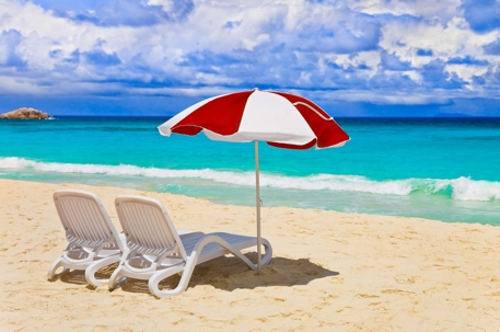 Two white lounge chairs and a red and white umbrella sit on a sunny beach.