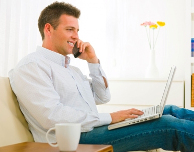 A man sits with a laptop while talking on a cellphone